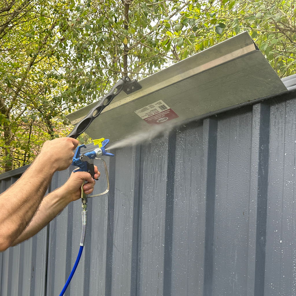 Tradie using an iQuip aluminium spray shield to protect gutters while airless spraying a fence