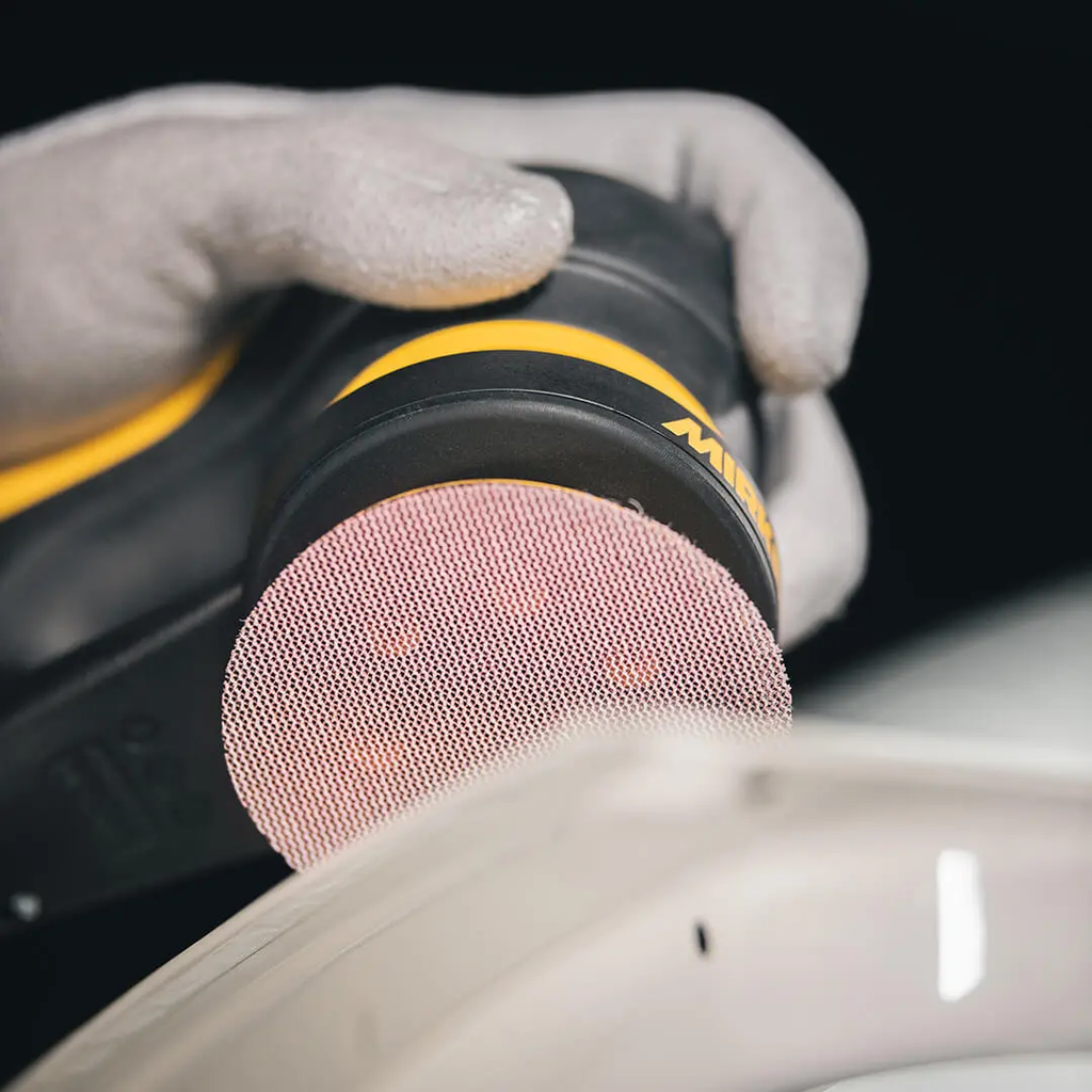 Tradie using a compact Mirka sander with a 77mm Abranet Ace disc on a curved panel