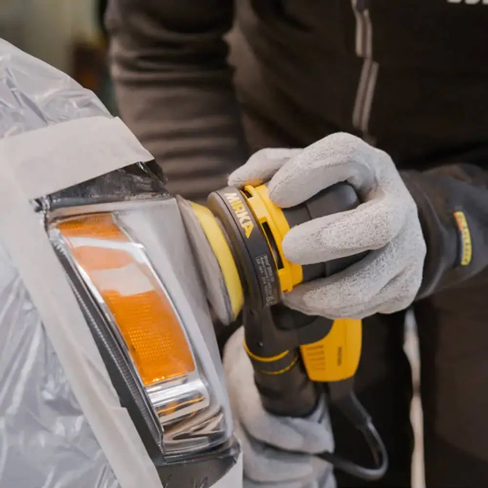 Professional using a 77mm Mirka DEROS II sander for automotive headlight restoration